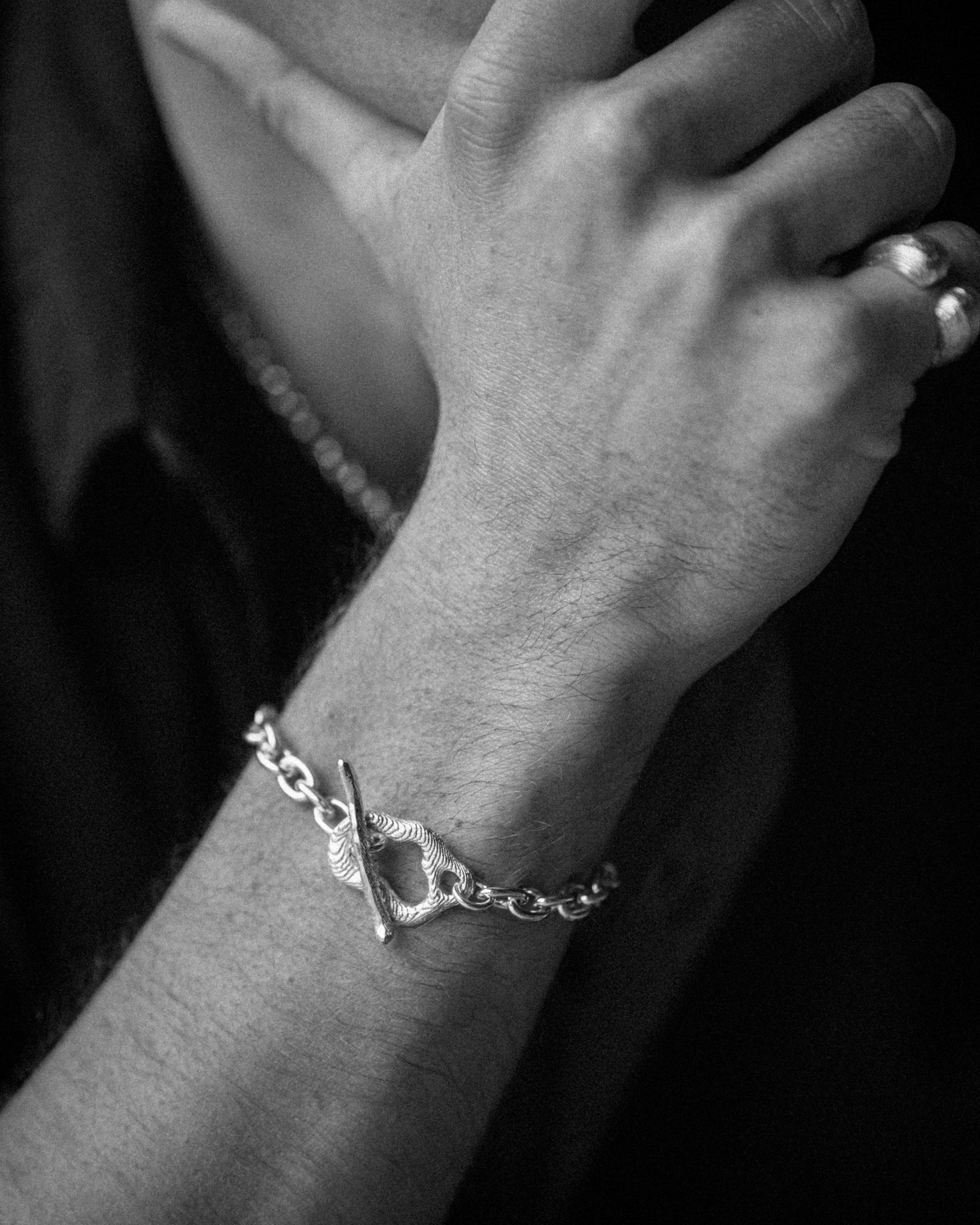 Close-up of a male model’s wrist wearing a bracelet with organic toggle links connected by a substantial cable chain