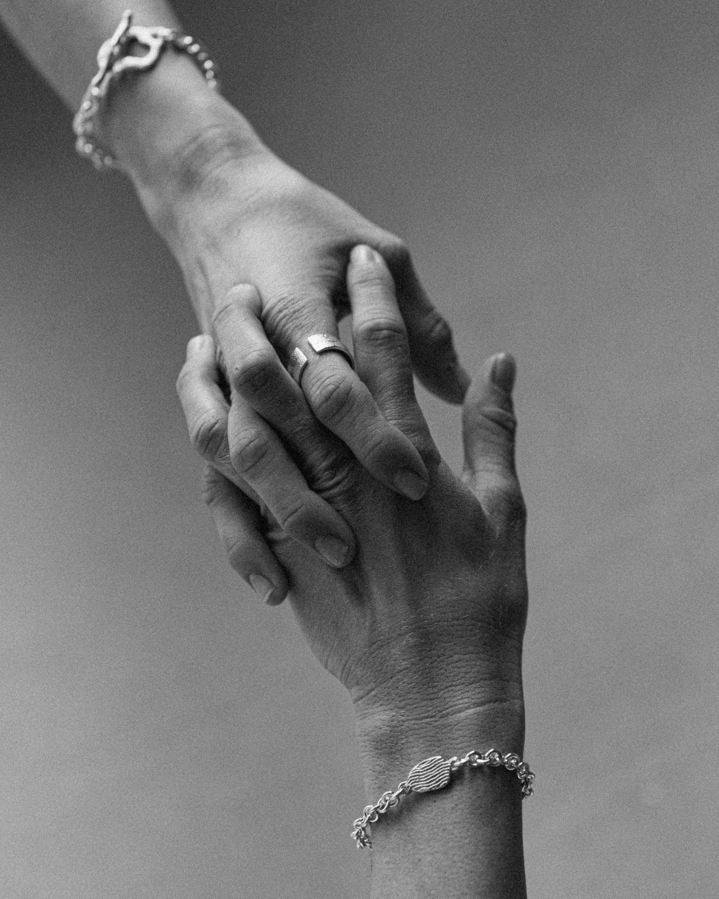 A person’s hand gently holding another’s hand, wearing a sterling silver tidal tab chain bracelet with a textured, wavy centerpiece