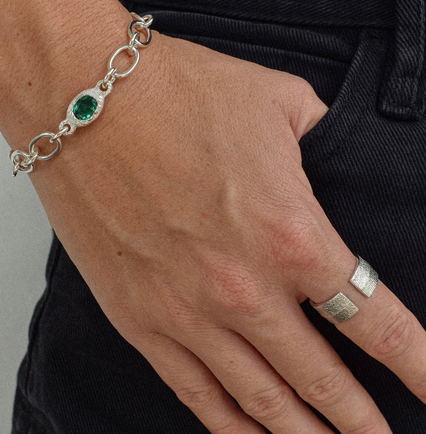 A model wearing a sterling silver bracelet on the wrist, featuring an emerald gemstone as the centerpiece, highlighting the vibrant green stone