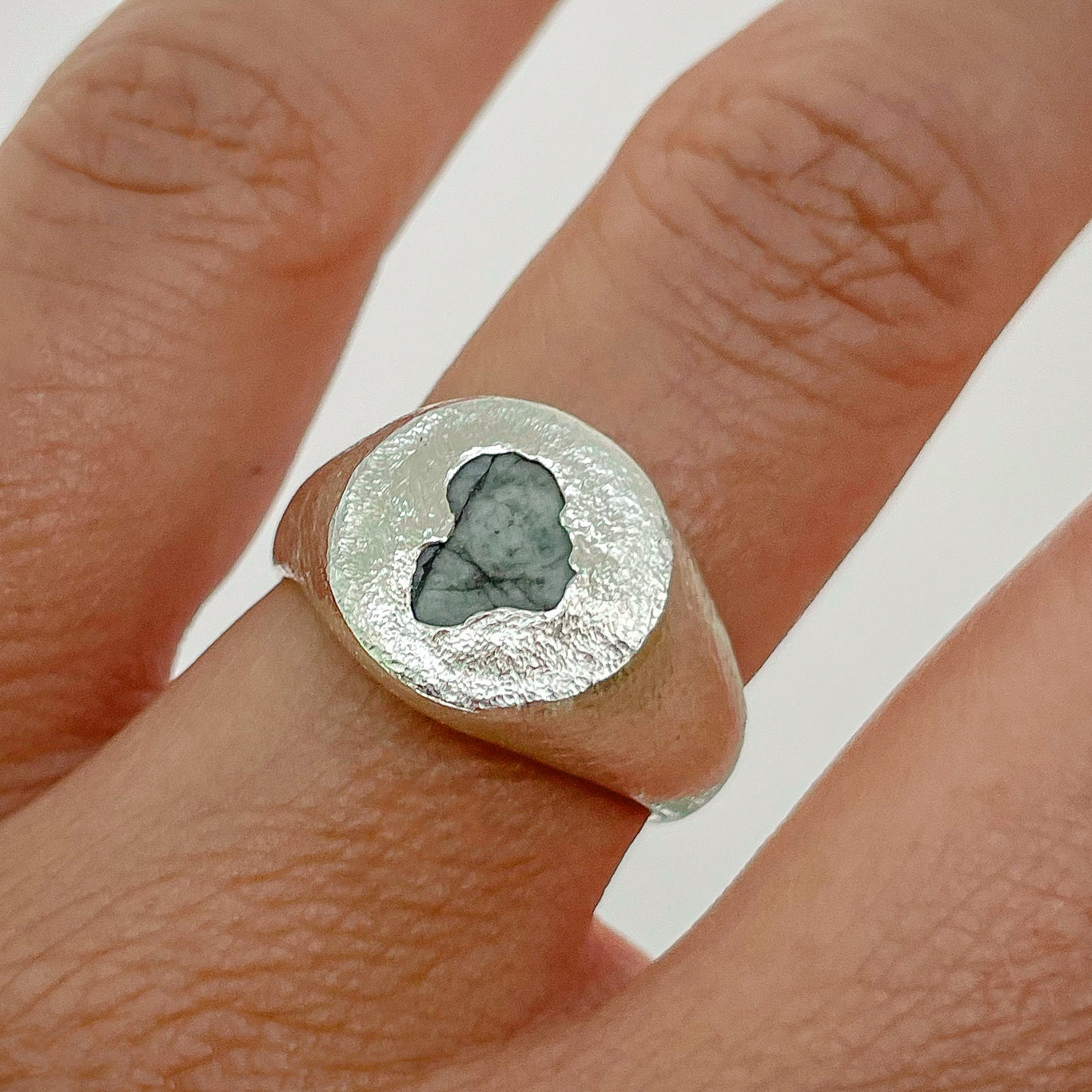 Sterling silver circle signet ring set with a raw emerald, worn on hand