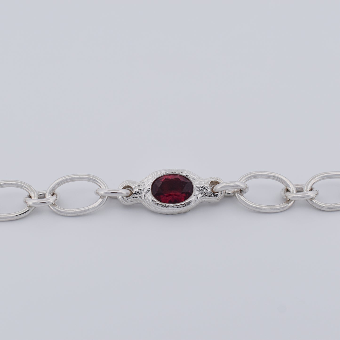 Close‑up of a sterling silver chain bracelet showing the oval textured centerpiece set with a deep red ruby