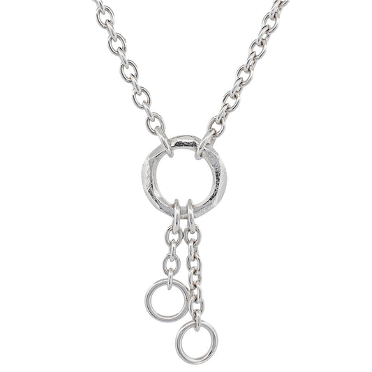 A contemporary sterling silver necklace featuring a bold, sculptural o-ring centerpiece. Two delicate cable chains cascade from the ring, each adorned with mini o-rings