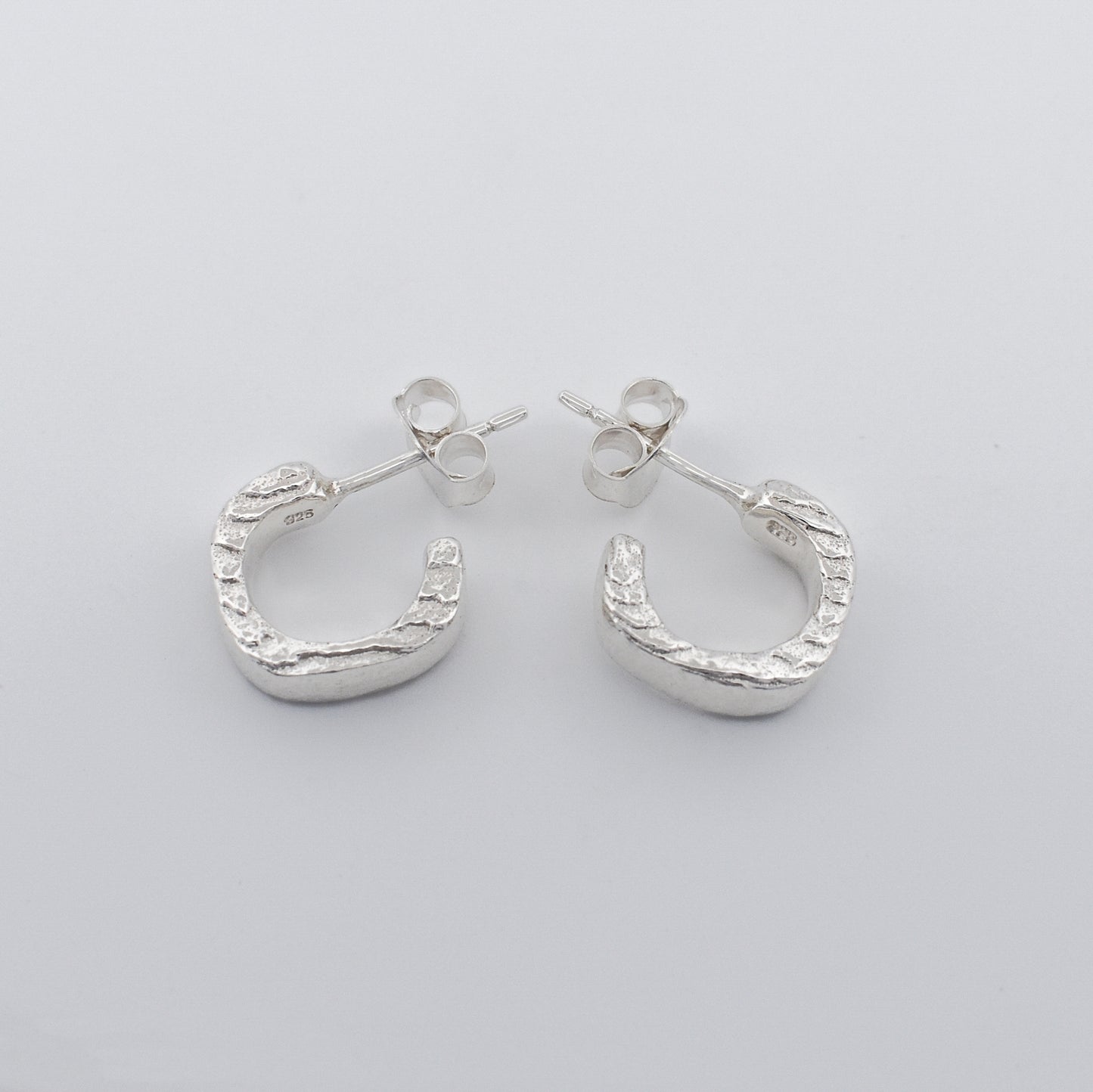 Detailed close‑up of hoop earrings featuring a striking textured finish and polished clean sides