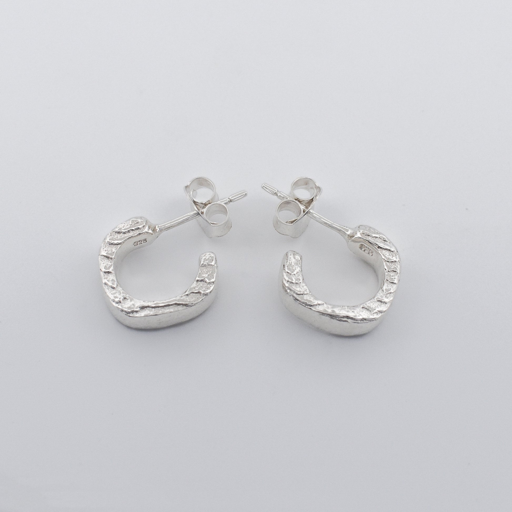 Detailed close‑up of hoop earrings featuring a striking textured finish and polished clean sides