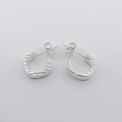 Detailed close‑up of hoop earrings featuring a striking textured finish and polished clean sides